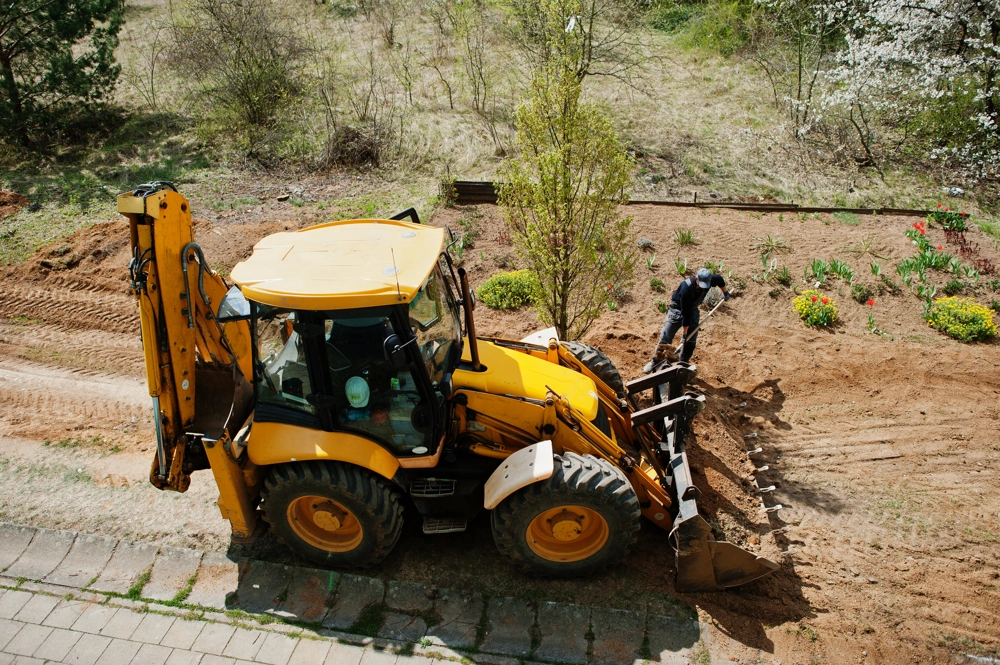 Koparko-ładowarka i pracownik wyrównują glebę podczas niwelacji terenu